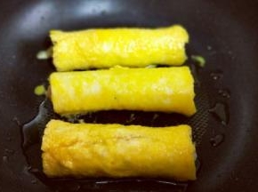 沾满蛋液的鲜虾吐司卷，放入平底锅中，刷上少许玉米油。