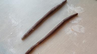 16．取适量的杏仁膏搓成长条，蘸上融化的黑巧克力，粘在房屋边缘的缝隙处，放置半小时巧克力凝固后姜饼屋就做好了。