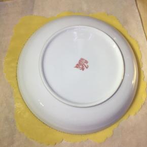 拆一张和烤盘一样大的油纸。醒好面后，取一个面团放油纸上，轻轻擀平，然后找一个八寸盘子（一般情况下家里日常用的盛菜盘子都是八寸的）扣在上面，然后用牙签绕盘子周边画一圈。取下盘子