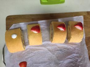 待蛋糕冷却后切出形状，将草莓切成两半，将草莓下面切平，挤上奶油，沾在蛋糕卷上当帽子