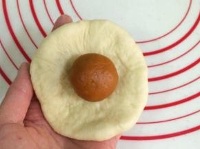 取一份松弛好的面团，擀成圆形片状，放上一份南瓜馅。