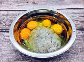 把鸡蛋磕入盛有鲜虾皮的容器里。