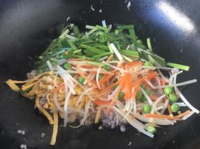 放入绿豆芽、胡萝卜丝、韭菜、豌豆，翻炒均匀。