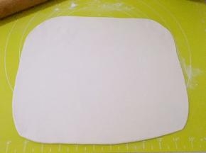 揉面垫撒点干粉，将松弛好的面团尽量擀成长方形，大小是冷冻黄油的两倍