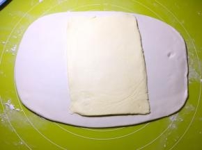 用剪刀裁破保鲜膜，将黄油片放在擀好的面片中间，黄油拿出来后很容易软化，这一步尽量动作快一点