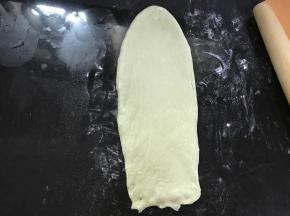 松弛后的面团擀成椭圆形，翻面后压薄长底边。