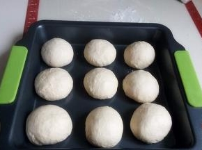 再次按压排气，分割为9份，每个约71克，滚圆，放入烤盘中