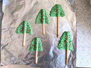 如图所示把巧克力挤刀饼干棒上，做成圣诞树的样子，撒上彩珠糖，放入冰箱冷藏