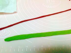 绿色面团擀薄，然后把深红曲面团搓成细条，放在蓝面片上，再用擀面杖擀平，切成长条，做围巾。