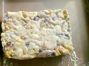 折叠均匀后放入烤盘里整形。可以借助刮板压实，但不要压的太薄，至少3cm厚。趁余温在雪花酥表面撒一层奶粉。