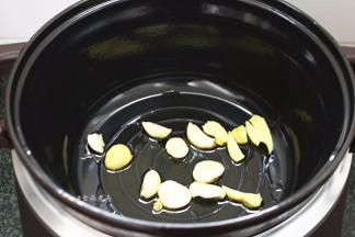 珐琅电炖锅通电，选择红烧功能键，倒入食用油，加热片刻后倒下蒜片和姜片