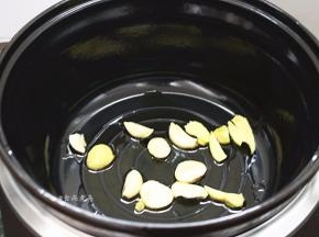珐琅电炖锅通电，选择红烧功能键，倒入食用油，加热片刻后倒下蒜片和姜片