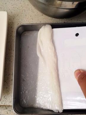 用取盘夹将盘子取出，一只手隔着湿抹布拿住托盘，另一只手用刮板把肠粉刮起来放到碟子里。