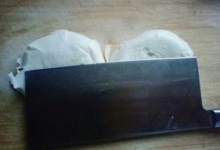 一个大白馒头，用刀身将其压扁。再次用刀身压切好的馒头片。将压扁的馒头丁切块。