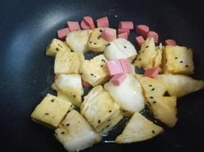 起油锅，油温7成时加入裹好鸡蛋液的馒头丁，中小火煎。加入切好的火腿肠。