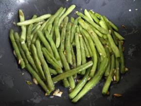 倒入豆角，改中火，在热油中翻炒，不时用锅铲压一下豆子，让豆子表面被烫起泡，微微出现焦痕。