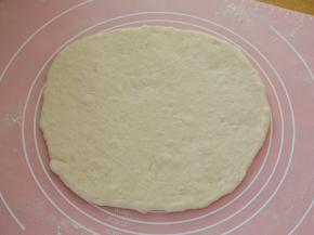 14.取一份面团抻成大饼，抻的水平有限就用擀面杖擀几下，就这样不规则的就好，不要擀的太圆，这就是这种披萨的特殊之处。