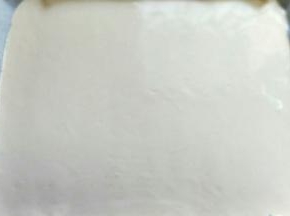 用刮板将蛋糕糊刮平，烤盘垂直震几下，震出气泡。