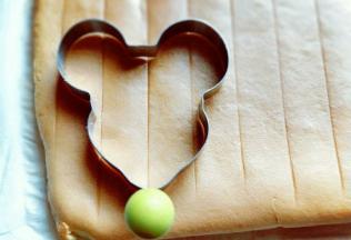 蛋糕烤好后，戴上隔热手套迅速取出烤盘，垂直摔一下，震出热气，趁热撕下油纸，翻面朝上，撕掉油纸后马上将蛋糕翻面，正面朝上，不然水蒸气加热气会导致蛋糕皮被粘掉。 之后用模具压出米老鼠的图案即可，没有模具的可以用碗压圆形，或者直接用刀切片都可以。