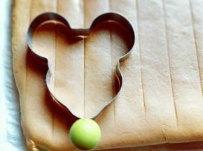 蛋糕烤好后，戴上隔热手套迅速取出烤盘，垂直摔一下，震出热气，趁热撕下油纸，翻面朝上，撕掉油纸后马上将蛋糕翻面，正面朝上，不然水蒸气加热气会导致蛋糕皮被粘掉。 之后用模具压出米老鼠的图案即可，没有模具的可以用碗压圆形，或者直接用刀切片都可以。