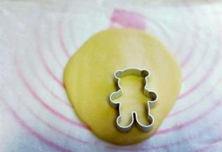 取下上面的油纸，用小熊模具压出小熊图案来，小心取下小熊饼干，放入烤盘中，将面团全部压完。