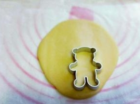 取下上面的油纸，用小熊模具压出小熊图案来，小心取下小熊饼干，放入烤盘中，将面团全部压完。