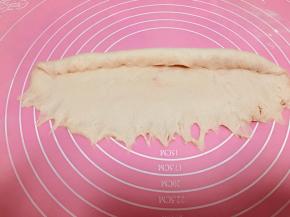 翻面，将面团横过来放。拍薄下侧。从上往下卷，边卷边按压。收口放在底部。将长条两头收尖，整体粗度搓一致。正面喷水，沾酥粒。