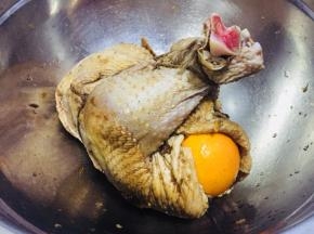 取出腌好的鸡，取一部分蔬菜塞在鸡肚子中，然后用一颗橙子塞在出口处。将鸡身反过来，鸡胸朝上，然后用细线将鸡腿捆绑起来如图