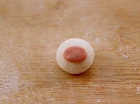包如馅料揉圆后、取一点粉色面团揉成长圆形、粘点水粘在白色面团上做鼻子
