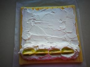 将放凉后的蛋糕再次倒扣，有图案的一面朝下，表面涂抹一层淡奶油，靠近身体的一端，要稍微多一些奶油，上面摆放猕猴桃，用淡奶油将猕猴桃盖住。