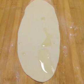 取一个剂子揉几下后擀成牛舌状，尽量擀薄一点，之后把油酥糊抹在面饼一半