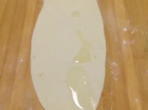 取一个剂子揉几下后擀成牛舌状，尽量擀薄一点，之后把油酥糊抹在面饼一半