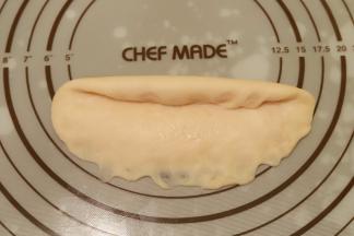 取一小份面团，擀成牛舌状，翻面，从上往下卷，下面用手指轻压，收口捏紧