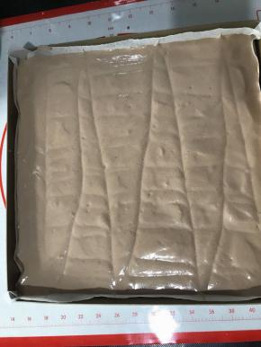 翻拌均匀，记得从底部充分翻拌，以免蛋黄糊残留在盆底。倒入铺了油纸的烤盘中，刮板抹平表面，并用牙签划几下，划出气泡。