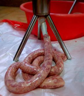 接下来开始灌肠，先用灌肠工具放进细肠口，然后开始放灌肠器里塞肉，然后用它的“黄金搭档”来推肉，这样一条条的腊肠就灌进去。