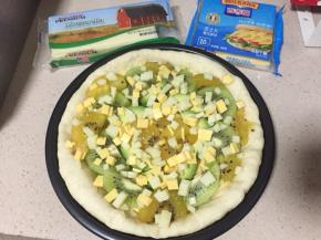 取一片百吉福芝士放在面皮上，在平铺上奇异果、牛油果，最后铺上马苏里拉奶酪碎和切丁的百吉福芝士片