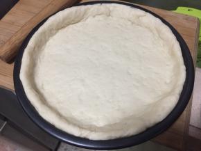 面团按扁，擀压成比披萨盘大一圈的面皮，将面皮覆盖在模具上整形