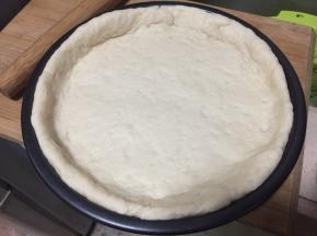 面团按扁，擀压成比披萨盘大一圈的面皮，将面皮覆盖在模具上整形