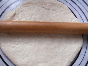 擀面杖涂抹一点黄油、防粘，取出面团，在案板上滚圆排气，盖上保鲜膜静置松弛15分钟，再用擀面杖擀薄至2厘米左右厚的圆饼