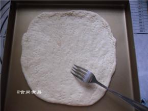 将面饼放在烤盆上，用手指将饼的边缘尽量压薄、用叉子在面饼的表面戳些小孔，帮助排气