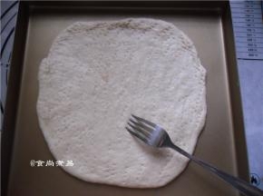 将面饼放在烤盆上，用手指将饼的边缘尽量压薄、用叉子在面饼的表面戳些小孔，帮助排气