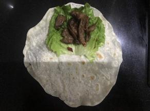 面饼上半部分放一张生菜叶，加勺炒好牛肉，包起来