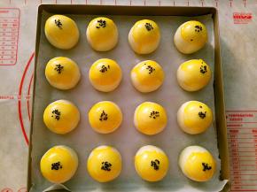 包好的蛋黄酥收口朝下，整齐地摆放在烤盘里。表面刷上蛋黄液点缀上黑芝麻。
