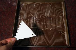 将可可蛋糕糊借助刮刀抹平在油纸上。然后用锯齿刮刀在面糊上划出纹路，放冰箱冷藏备用。