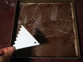 将可可蛋糕糊借助刮刀抹平在油纸上。然后用锯齿刮刀在面糊上划出纹路，放冰箱冷藏备用。