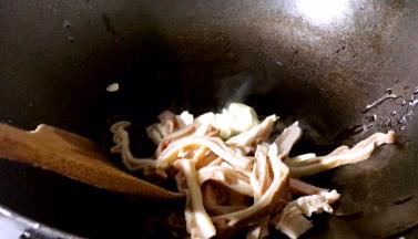 锅烧热油，放入蒜片和猪肚条，一起炒出香味