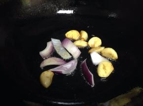 小火倒入蒜瓣，煎至表面微黄时下入一半的洋葱煸出香味