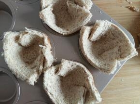 擀好的土司片放入杯子蛋糕模具中。边缘折一下再放进去，然后用手把底部压好。