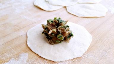 取一张包子皮，中间放入适量肉馅。