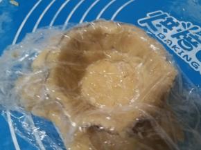 揭掉一面的保鲜膜，将另一面有保鲜膜的面朝上盖在模子里。用手按压，使饼皮跟模子紧密的贴合在一起。